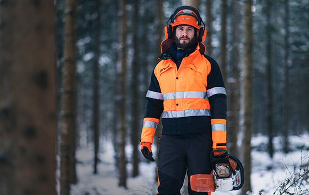 A logger walking in the forrest with a chainsaw in his hand